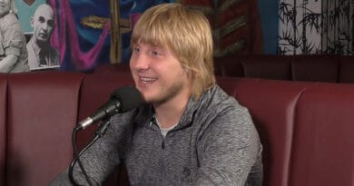 Bildbeskrivning: En person med ljust hår och grå tröja sitter vid en mikrofon, ler och pratar. Bakgrunden har dekorerade väggar med färgglada mönster. Bilden förmedlar en vänlig och avslappnad atmosfär. Kategori: Underhållning. Nam