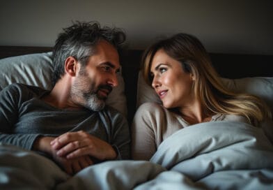 Denna bild visar ett par i en säng som tittar kärleksfullt på varandra. Mannen har grått hår och skägg, medan kvinnan har långt, blont hår. Deras avslappnade kroppsspråk och mjuka leenden skapar en varm och intim stämning. Detta foto