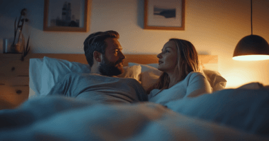 I bilden ser vi ett par i ett mysigt sovrum, som njuter av en lugn stund i sängen. Den dämpade belysningen från en hängande lampa skapar en varm och avkopplande atmosfär. Målningar på väggen och prydnadsföremål på byrån först