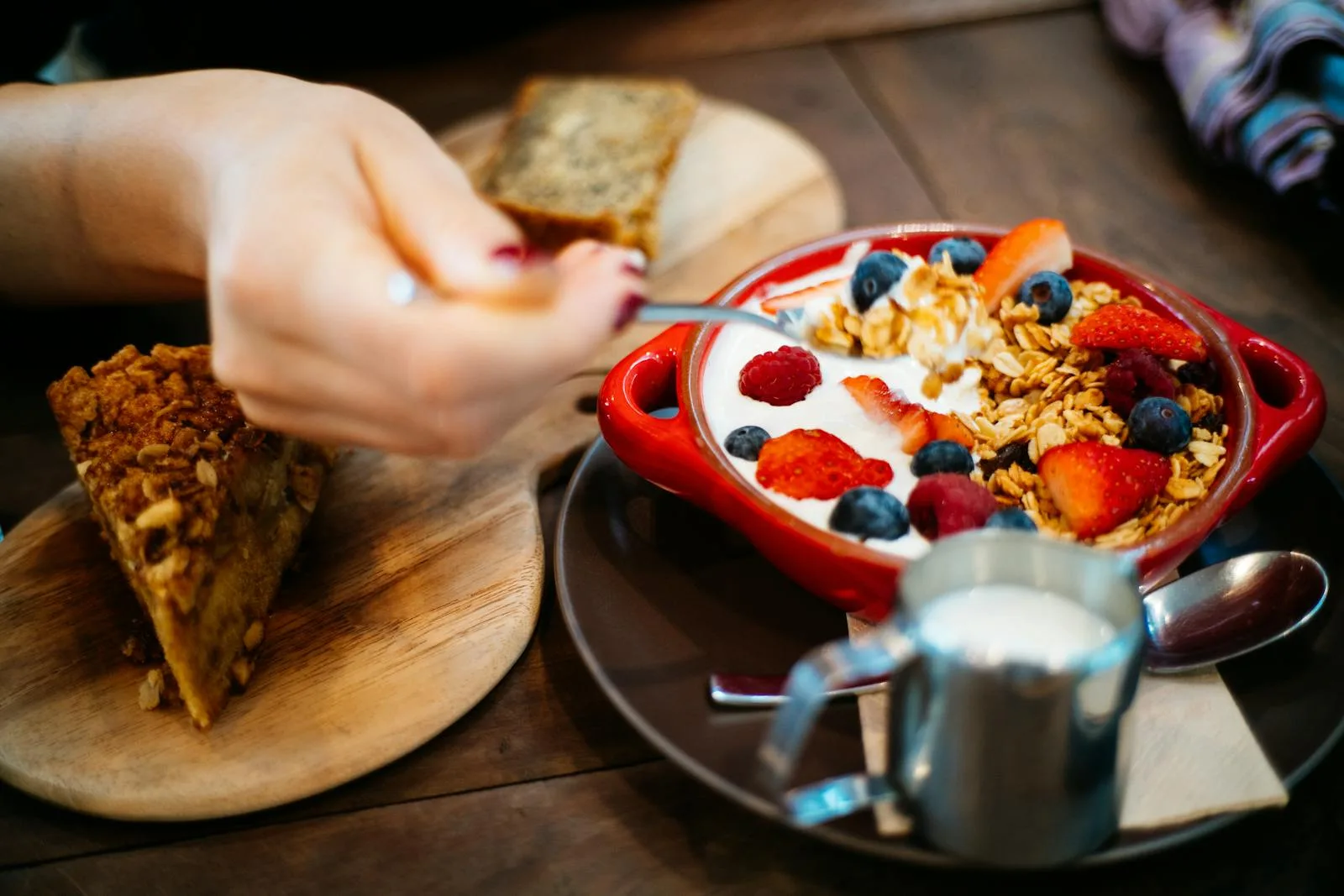 Close-up of a breakfast setting with granola, fresh berries, and a slice of cake.