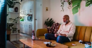 A man relaxes on a sofa with a beer, watching TV in a cozy living room.