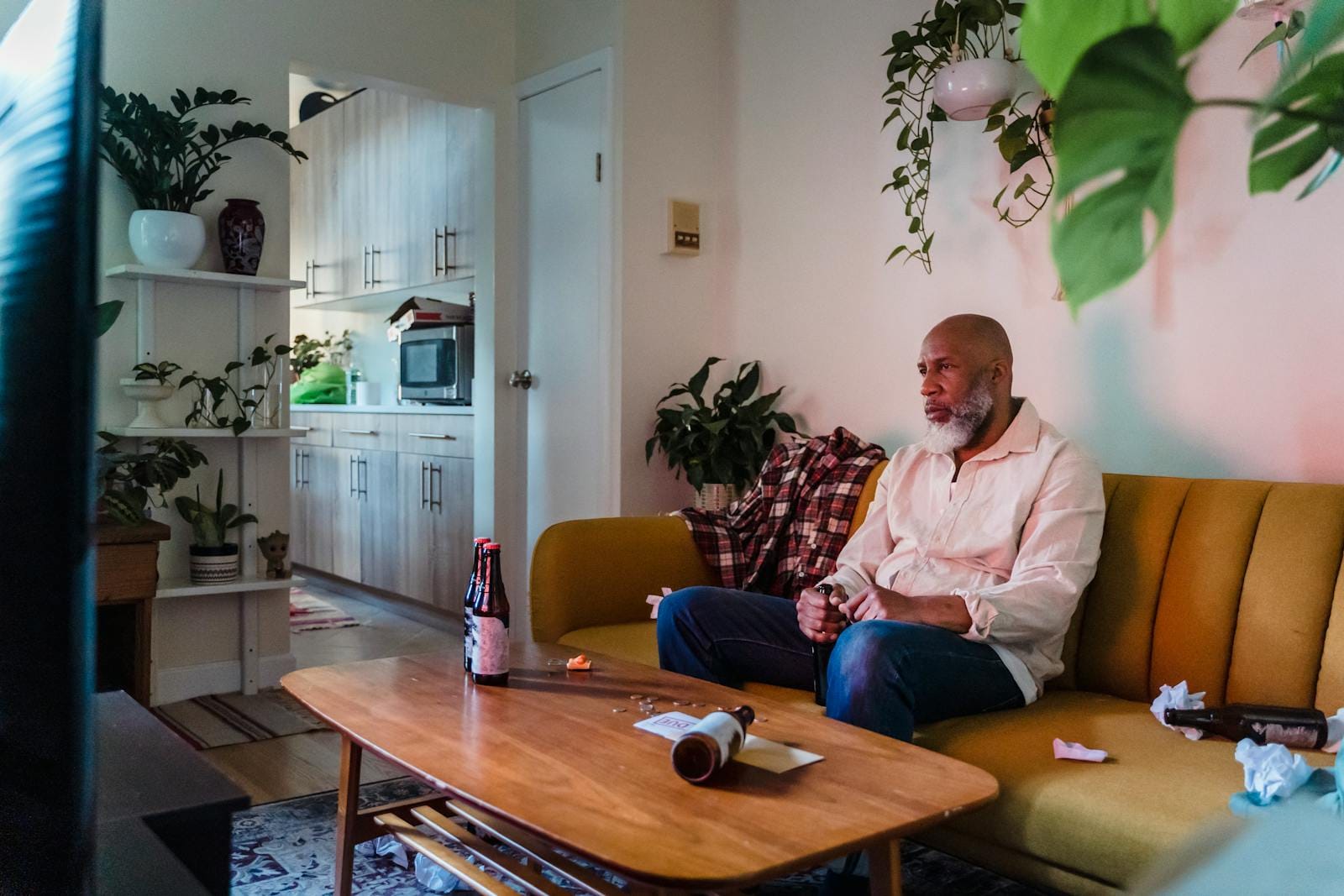 A man relaxes on a sofa with a beer, watching TV in a cozy living room.