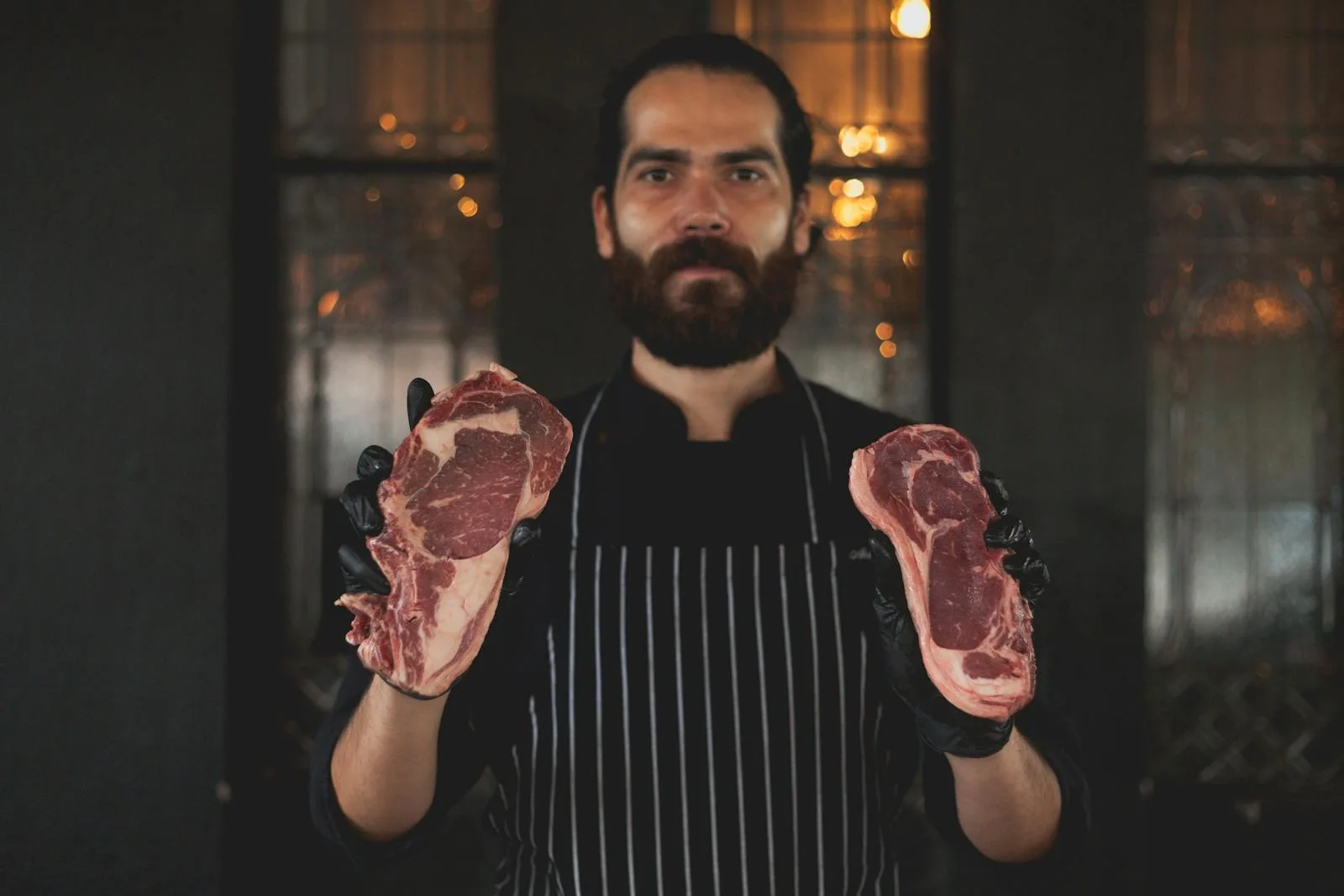 Bearded chef showcasing raw steaks, perfect for culinary arts and cooking themes.