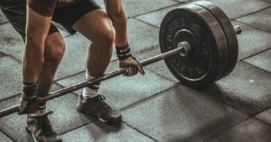 A focused weightlifter prepares to lift a heavy barbell in an indoor gym setting.