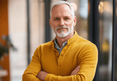 Jag är osäker på vem personen är, men jag kan beskriva bilden.Modern affärsman i en gul tröja med självsäker hållning i kontorsmiljö. Stilren och professionell framtoning. Midcent: Samhälle.