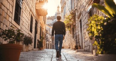 Midcent: En man promenerar längs en pittoresk stenlagd gränd i solnedgången, omgiven av charmiga, rustika byggnader och grönskande växter. Perfekt för resenärer som söker historisk atmosfär och natursköna vyer. Resa.