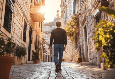 Midcent: En man promenerar längs en pittoresk stenlagd gränd i solnedgången, omgiven av charmiga, rustika byggnader och grönskande växter. Perfekt för resenärer som söker historisk atmosfär och natursköna vyer. Resa.