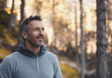 Midcent: Vuxen man njuter av en fridfull promenad i skogen, omgiven av höstens gyllene nyanser. Hans avslappnade uttryck speglar glädje och naturlig harmoni, vilket förmedlar en känsla av lugn och friskhet. Kategori: Hälsa.