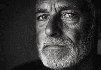 Svartvitt porträtt av en äldre man med intensiv blick och skägg, fångar djupa känslor och livserfarenhet. Midcent. Kategori: Samhälle.