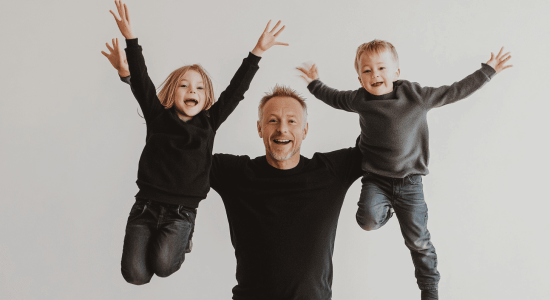 Midcent: En glad familjestund med skratt och lek, där en man lyfter två glada barn i luften, symboliserar kärlek och gemenskap. Perfekt för att illustrera familjelivets glädje. Kategori: Samhälle.