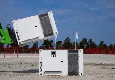 Midcent: Bilden visar en mobil energi- och kraftlösning från Northvolt. Perfekt för hållbar energiutveckling, den dokumenterar installation eller flytt av batterisystemet i en industriell miljö med klarblå himmel. Kategori: Teknik.