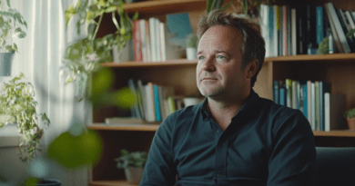 Bild av en man i ett hemtrevligt kontor med gröna växter och böcker. Han verkar reflekterande och avslappnad, omgiven av lugnande miljö. Perfekt för artiklar om arbetsmiljö och inredningstrender.Midcent - Samhälle.