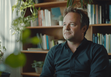 Bild av en man i ett hemtrevligt kontor med gröna växter och böcker. Han verkar reflekterande och avslappnad, omgiven av lugnande miljö. Perfekt för artiklar om arbetsmiljö och inredningstrender.Midcent - Samhälle.