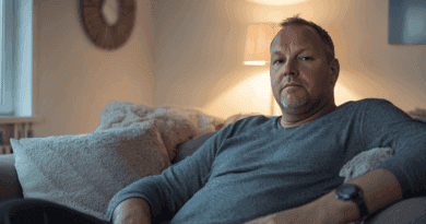 Bekväm atmosfär i ett modernt vardagsrum med mjuka texturer. En man sitter avslappnat på soffan med avslappnad belysning. Perfekt för en lugn kväll hemma. Midcent - Samhälle.