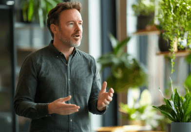 Midcent presenterar en avslappnad interiör med frodig grönska, där en man gestikulerar engagerat. Fokus på miljövänliga kontorslösningar och naturlig inredning. Harmoniskt och inspirerande arbetsrum för kreativitet och produktivitet.Kategori: Samhälle.