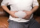 A close-up view of a man holding his tummy while sitting on a couch, highlighting lifestyle choices.