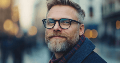 Jag vet inte vem personen på bilden är. Den föreställer en man med glasögon och skägg, klädd i en vinterscarf i en urban miljö med bokeh-effekt. Midcent, kategori: Samhälle.