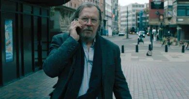 En medelålders man använder mobiltelefon på en stadsgata, iklädd en elegant kavaj och halsduk. Urban miljö med moderna byggnader i bakgrunden. Midcent. Kategori: Samhälle.