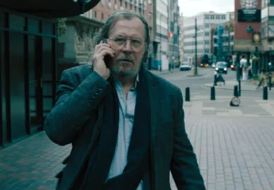 En medelålders man använder mobiltelefon på en stadsgata, iklädd en elegant kavaj och halsduk. Urban miljö med moderna byggnader i bakgrunden. Midcent. Kategori: Samhälle.