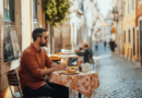 En medelålders man njuter av sin måltid vid ett kafé i en charmig, solig gränd. Bilden fångar avslappning och lokal kultur. Midcent: Resa.