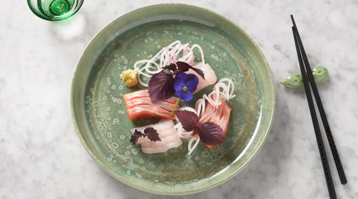 Midcent presenterar en elegant tallrik sashimi, vackert arrangerad med färska fiskbitar, wasabi och dekorativa blommor på en grön tallrik. Perfekt för den matintresserade som söker en estetisk kulinarisk upplevelse. Kategori: Mat.