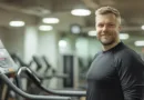 Midcent: En medelålders man i träningskläder ler bredvid en löpband på ett gym, med fokus på hälsosam livsstil och träning. Hälsa.