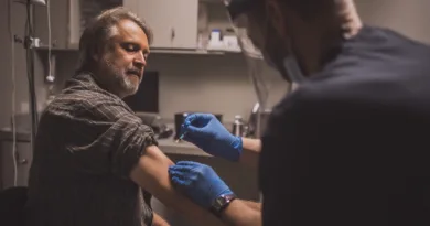 En medelålders man får en injektion i en klinikmiljö, med fokus på sjukvård och säkerhet. Midcent. Kategori: Hälsa.