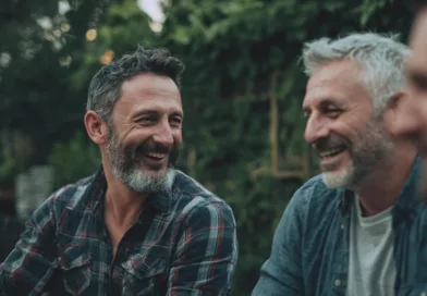 Midcent: Tre medelålders män skrattar hjärtligt tillsammans i en utomhusmiljö, omgivna av grönska. Glädje och gemenskap i fokus. Underhållning.