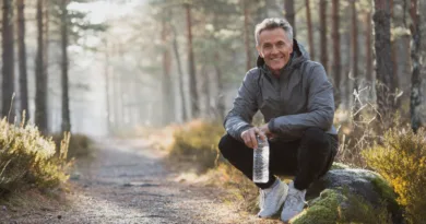Midcent: En vuxen man sitter på en sten i skogen med en vattenflaska. Hälsa.