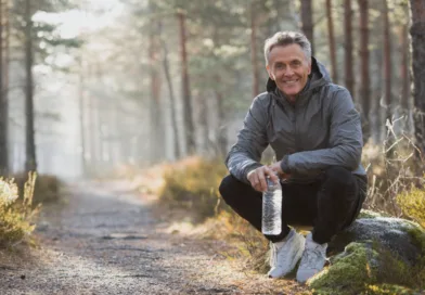 Midcent: En vuxen man sitter på en sten i skogen med en vattenflaska. Hälsa.