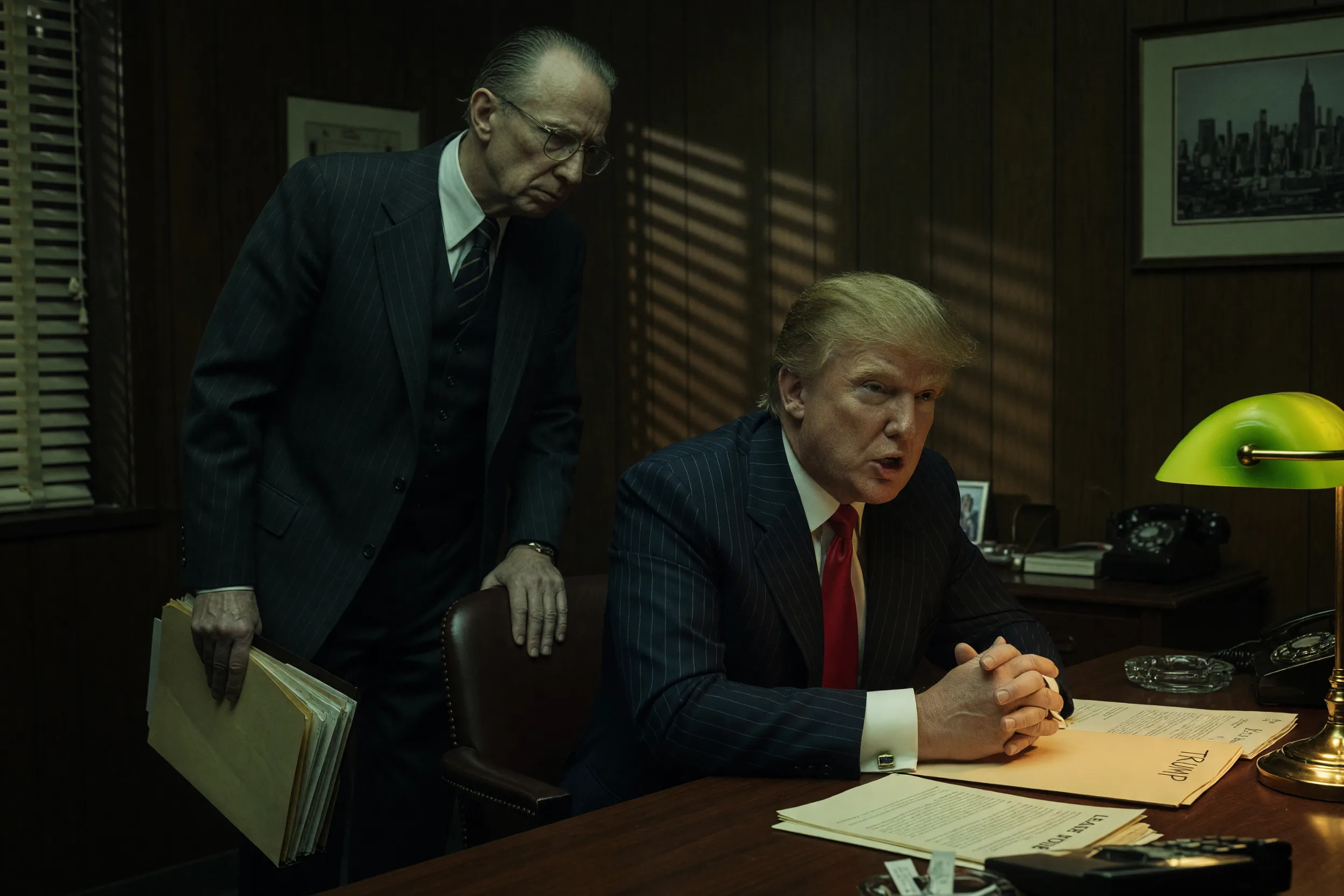 En advokat står i skuggorna bakom en ung Donald Trump.