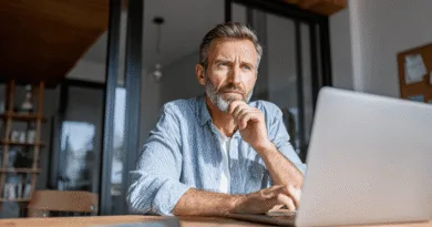 Midcent: En medelålders man sitter vid en dator, djupt försjunken i tankar. Han bär en randig skjorta och betraktar skärmen i ett modernt kontor eller hem. Perfekt för teman inom arbete och fokus. Kategori: Ekonomi.