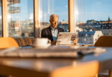 En medelålders man sitter vid ett bord i ett soligt rum och läser en tidning. Bilden förmedlar lugn och fokus i en stadsnära miljö. Midcent. Kategori: Samhälle.
