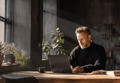 Midcent: En medelålders man i en stilfull interiör, omgiven av krukväxter, arbetar fokuserat på sin laptop vid ett solbelyst skrivbord. Perfekt plats för kreativitet och produktivitet. Kategori: Teknik.