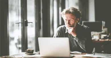 En medelålders man arbetar fokuserat vid en dator i ett stilfullt kontor. Han dricker kaffe medan han går igenom viktiga dokument. Bilden förmedlar en atmosfär av professionalism och koncentration.Midcent: Ekonomi.