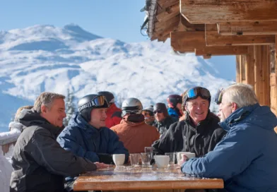 Midcent: En grupp medelålders män njuter av en solig vinterdag på en skidort, samlade kring ett bord med varma drycker.