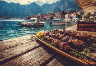 Midcent Mat: Kebabspett serverade vid en pittoresk kust med klarblått vatten och charmiga bergsbyar i bakgrunden. Upplev smaken av medelhavet och njut av en gastronomisk resa i solen. Perfekt för matentusiaster och semesterfirare.