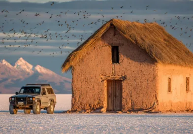Midcent Resa: Öde hus vid Salar de Uyuni, omgiven av Andesfjällen. En robust jeep står parkerad bredvid, omgiven av en flock fåglar som flyger över det vidsträckta saltfältet. Perfekt för äventyrsresor och naturälskare.