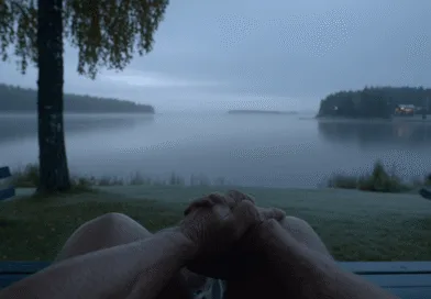 En medelålders man ser ut över en stilla sjö i gryningen, omgiven av dimma och en lugn atmosfär. Perfekt för avkoppling och eftertanke i naturens skönhet.Midcent, Resa.