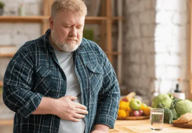 Midcent: En medelålders man med magont står i köket, omgiven av hälsosam mat som frukt och grönsaker. Han ser bekymrad ut och håller sig för magen. Bilden representerar hälsa och välbefinnande. Kategori: Hälsa.