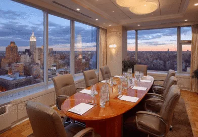 Midcent: Ett elegant konferensrum med panoramautsikt över en storstads silhuett i skymningen, vilket erbjuder en professionell atmosfär för företagsmöten. Rymlig interiör och modern inredning för en optimal arbetsmiljö. Kategori: Ekonomi.