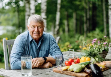 Jag kan inte identifiera personen, men här är en kortfattad beskrivning:En medelålders man sitter vid ett bord ute i naturen