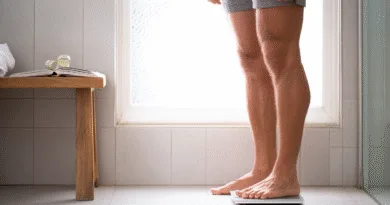 Midcent: En medelålders man står på en våg i ett badrum, bredvid ett måttband och en öppen bok, vilket illustrerar hälsomedvetenhet och viktkontroll. Kategori: Hälsa.