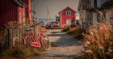 Midcent: En idyllisk svensk kustby med röda stugor, en rosa cykel lutad mot ett staket och en vintagebil i bakgrunden, fångar sommarkänslan perfekt. Fridfull atmosfär vid havet. Resa.