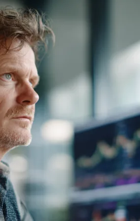 En medelålders man fokuserar på datorskärmar fyllda med aktiediagram i en modern kontorsmiljö. Bilden symboliserar