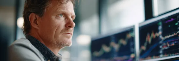 En medelålders man fokuserar på datorskärmar fyllda med aktiediagram i en modern kontorsmiljö. Bilden symboliserar