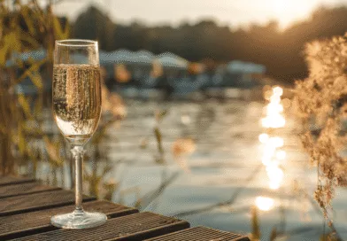 Midcent – Bilden visar ett glas champagne vid en sjö i solnedgång, vilket skapar en stämningsfull och avkopplande atmosfär. Perfekt för dem som söker njutning och lyx. Kategori: Resa.