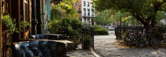 Upplev den charmiga atmosfären i en stadsmiljö med Midcent, där solens strålar belyser en mysig caféterass. Njut av en kopp kaffe i en lugn gata med grönska och cyklar i bakgrunden. Kategori: Samhälle.