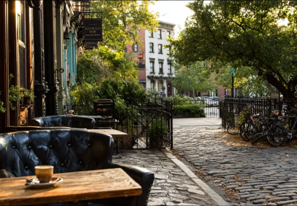 Upplev den charmiga atmosfären i en stadsmiljö med Midcent, där solens strålar belyser en mysig caféterass. Njut av en kopp kaffe i en lugn gata med grönska och cyklar i bakgrunden. Kategori: Samhälle.
