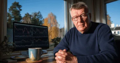 En medelålders man sitter vid ett skrivbord med en dator som visar aktiediagram. En kopp kaffe står bredvid. Man ser ett fönster med höstlöv i bakgrunden. Midcent. Kategori: Ekonomi.